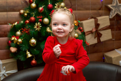 The girl laughs while playing near the christmas tree with gifts on the wall.