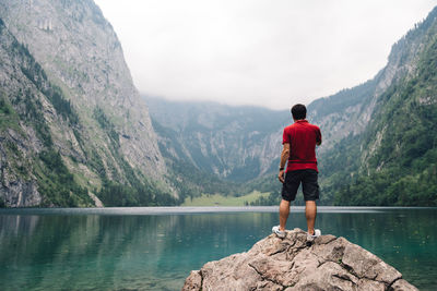 Rear view of man standing on rock by lake