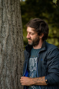 Young man looking away while standing in forest