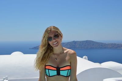 Portrait of smiling woman sitting on building by sea against clear blue sky