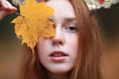 Close-up portrait of young woman holding maple leaf
