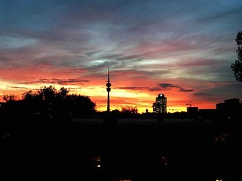 Silhouette of city against cloudy sky during sunset