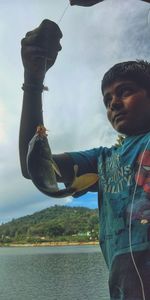 Man holding fish in lake against sky