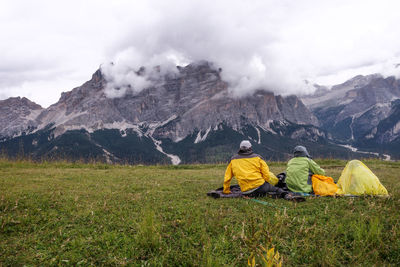 Rear view of men sitting on mountain against sky