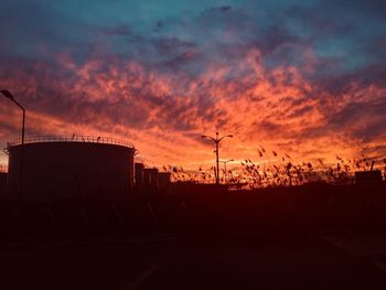 Silhouette of factory against sky during sunset