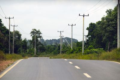 Road by electricity pylon against sky