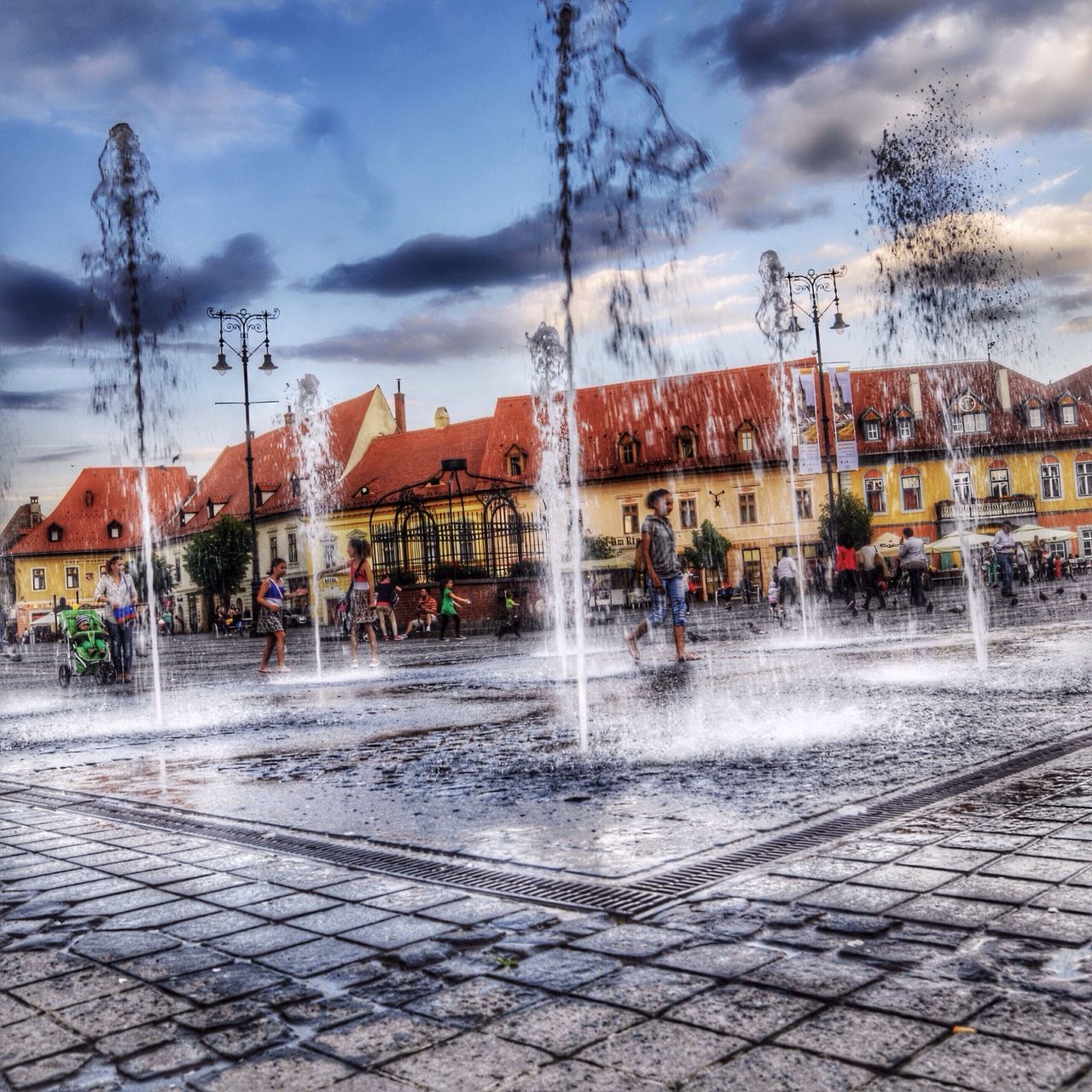 building exterior, sky, architecture, cloud - sky, built structure, street, cloudy, city, cloud, tree, road, sidewalk, outdoors, transportation, residential building, cobblestone, water, incidental people, residential structure, city street