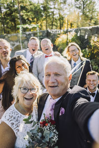 Cheerful newlywed senior couple taking selfie with family and friends at wedding