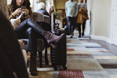 Low section of mid adult woman using mobile phone while sitting on chair in hotel lobby