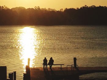Silhouette people by sea against sky during sunset