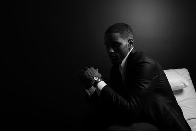 Thoughtful man wearing suit sitting on bed against wall