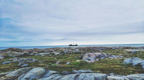 Scenic view of rocky shore and sea against cloudy sky