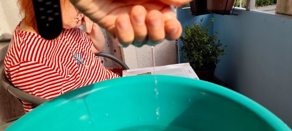 Close-up of water falling from hand in bucket with girl studying at background