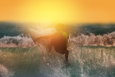 Man surfing in sea against sky during sunset