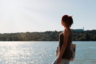 Redhead woman enjoying in sunlight by the river in summer day. copy space.