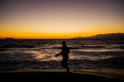 Silhouette man standing on beach against clear sky during sunset