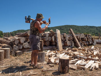 Side view of man carrying axes while standing against clear sky