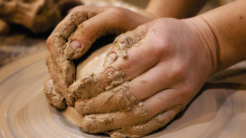 Cropped hands of craftsperson making clay product in pottery workshop