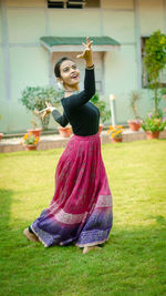 Young woman dancing on grassy field against building in yard