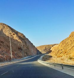 Road leading towards mountains against clear blue sky