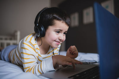 Focused little boy in casual wear browsing laptop while spending free time in bedroom at home