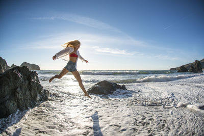 Teenage girl jumping off rock into surf at beach