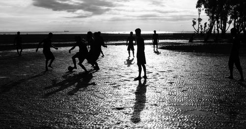 Silhouette people walking on beach against sky