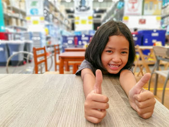 Portrait of smiling girl showing thumbs up at restaurant