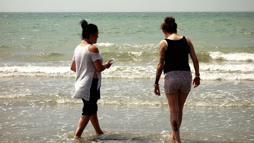 Friends walking at beach during sunny day