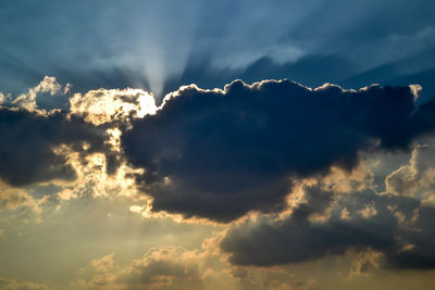 Low angle view of sunlight streaming through clouds