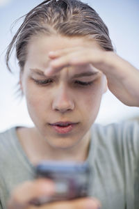 Young man shielding his eyes while using mobile phone against sky