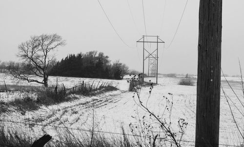 Electricity pylon by railroad tracks against sky during winter