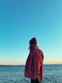 Rear view of woman standing at beach against clear blue sky