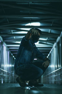 Full length side view of man holding camera while crouching on bridge