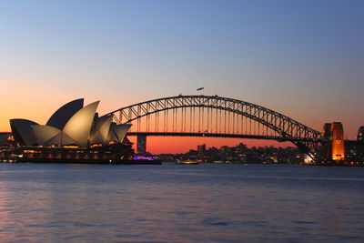 Opera house by harbor bridge at seafront during sunset