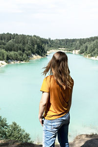 Rear view of woman standing by lake against sky