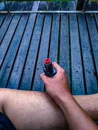 High angle view of man holding electronic cigarette while sitting on wood