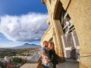 Side view of romantic couple standing by railing against sky