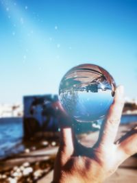 Close-up of hand holding crystal ball against sky