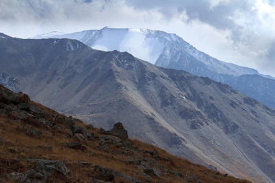 Three mountain ranges - grassy, rocky and with a glacier in autumn against a sky with clouds