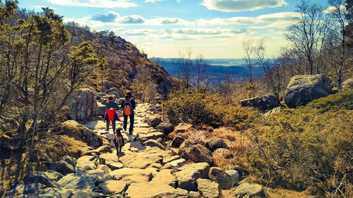 Rear view of people with dog on rock against sky