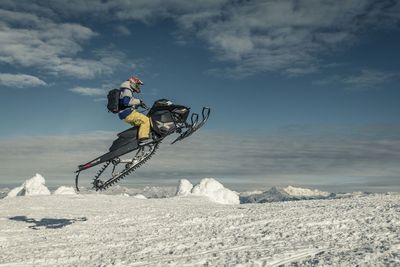 Side view of man snowmobiling on snowcapped mountain