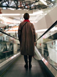 Rear view of woman standing on moving walkway in shopping mall