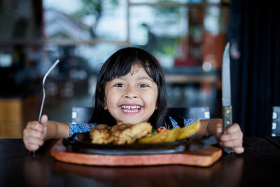 Close-up portrait of smiling girl with food on table in restaurant