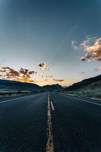 Road by mountains against sky during sunset