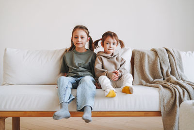 Cure two children girls sisters having fun on couch at the home