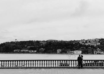 People on railing in city against sky