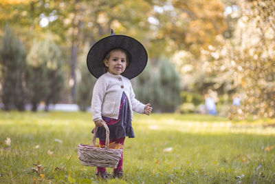 Portrait of cute girl wearing hat standing on grass at park
