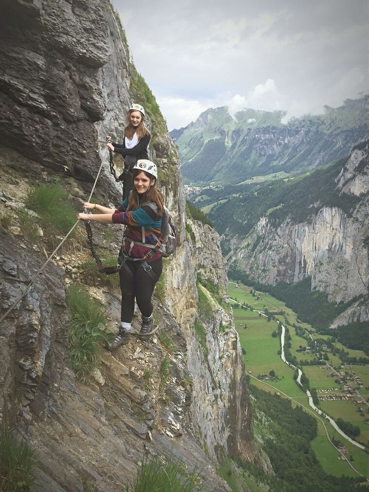 full length, young adult, lifestyles, leisure activity, casual clothing, person, looking at camera, mountain, portrait, young women, standing, smiling, front view, happiness, rock - object, sky