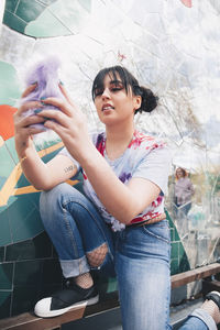 Young woman using mobile phone by mosaic wall